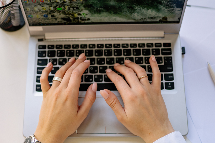Hands typing on a laptop keyboard while working online at a desk