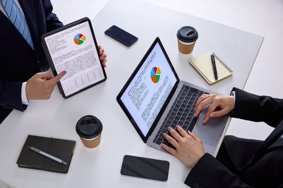 Finance professionals reviewing digital invoice reports on a tablet and laptop