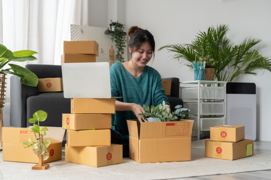 Small business owner packing products into cardboard boxes beside a laptop at home