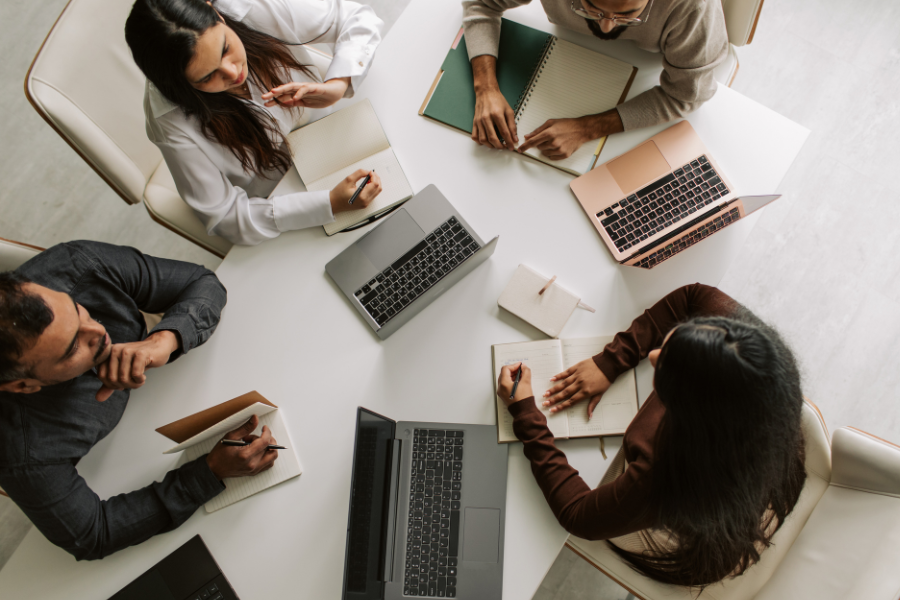 Diverse business team collaborating around a table with laptops, notebooks, and documents during a workplace meeting
