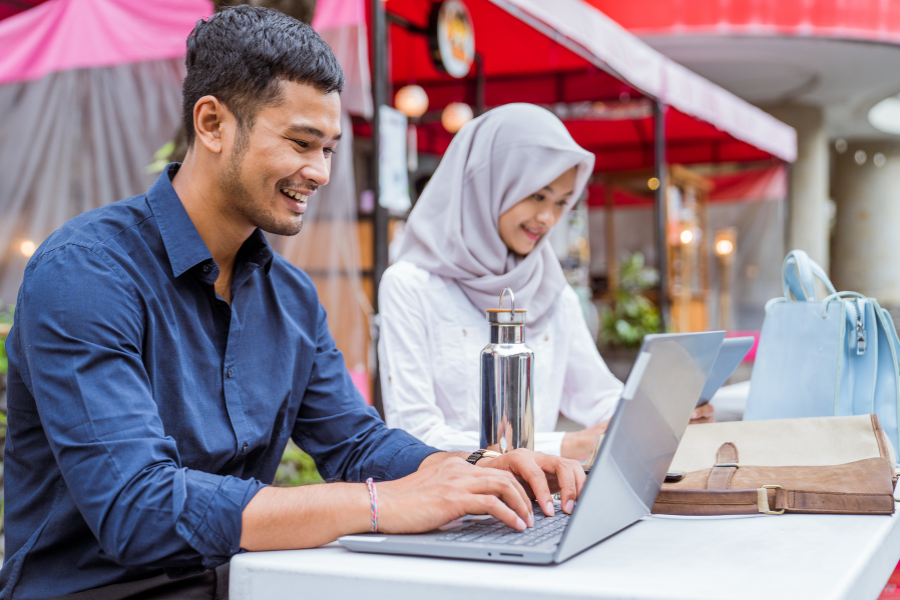 Two professionals working remotely on laptops at an outdoor café while collaborating on digital business tasks.